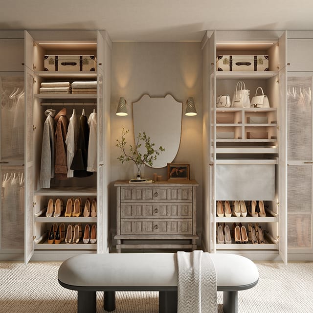 A refined walk-in closet featuring hanging clothes, shelves with shoes and handbags, storage boxes, and a central dresser topped with a decorative mirror and flanked by wall sconces.