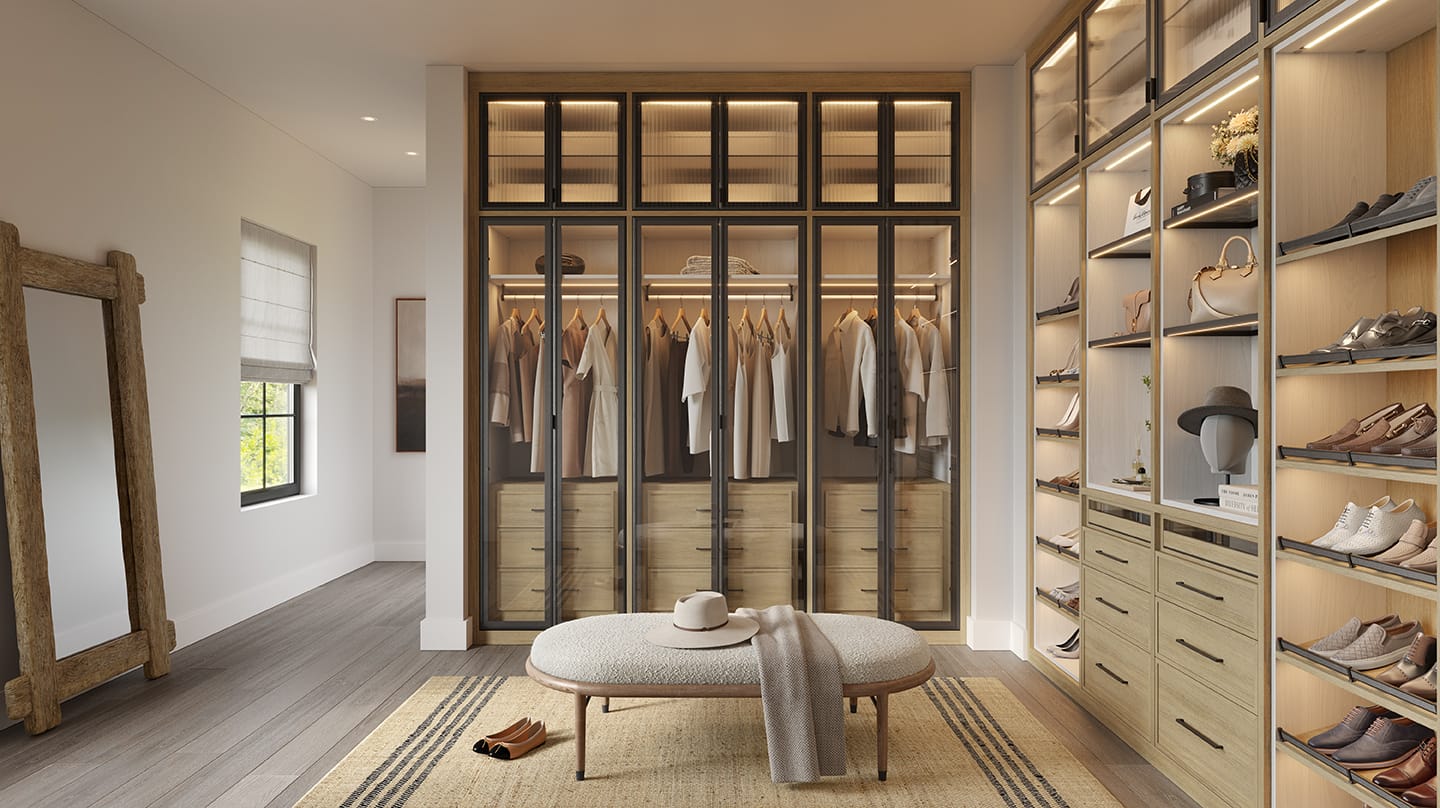 A stylish walk-in closet with wooden finishes, glass door cabinets displaying hanging clothes, open shelving for shoes and accessories, a large wall mirror, and a cushioned bench centered in the space.